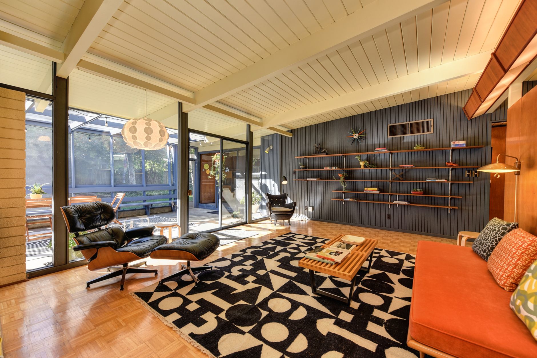 Eames lounge chair beneath beamed ceiling with glass wall beyond