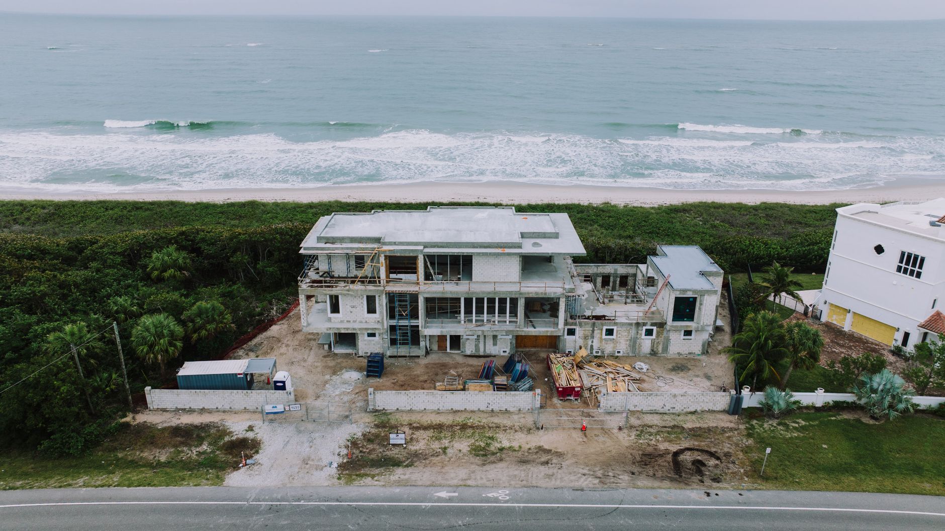 Aerial shot of a house under construction near the ocean with lush greenery.