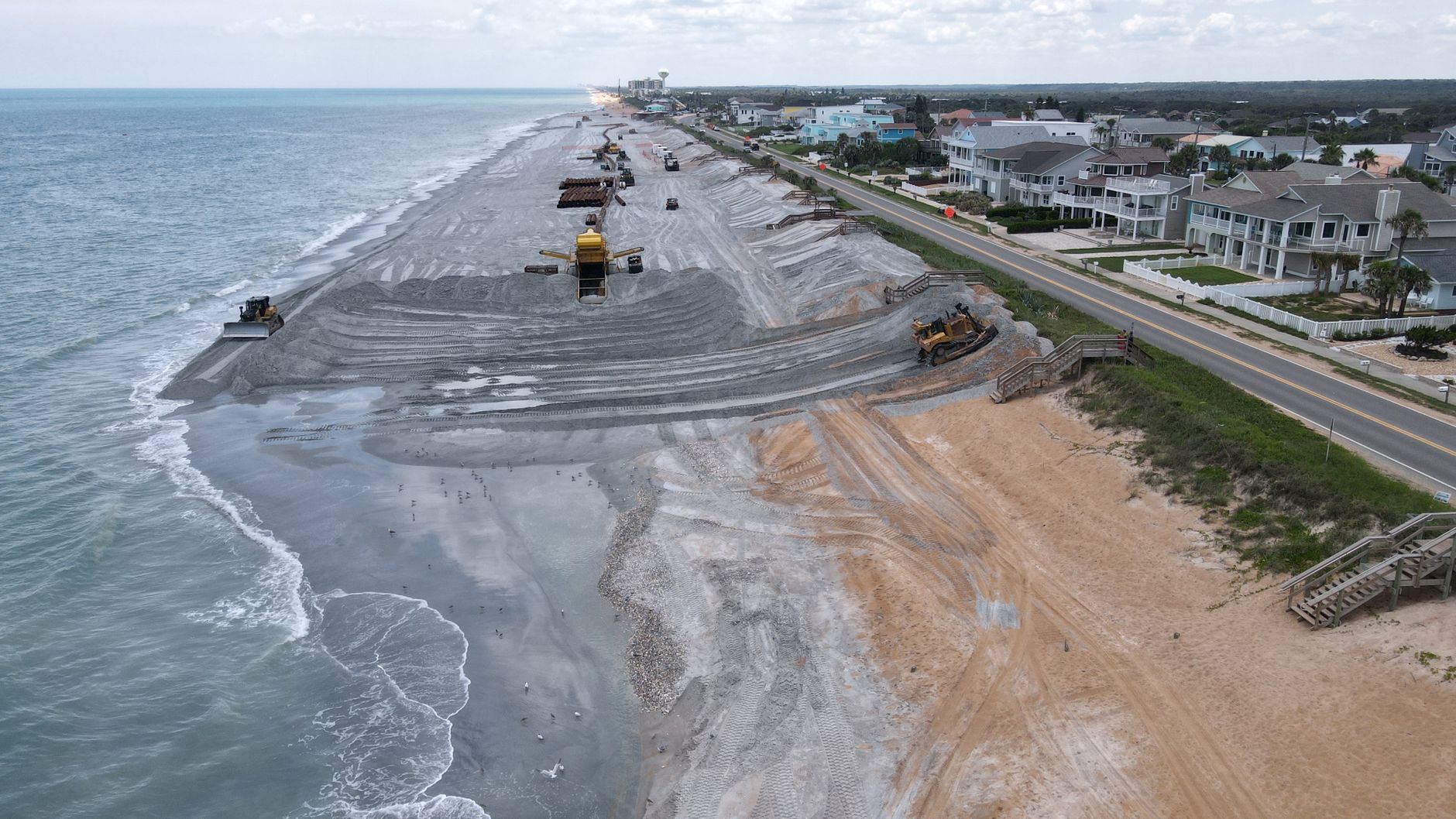 Aerial view of a beach restoration project with construction vehicles on the coastline.