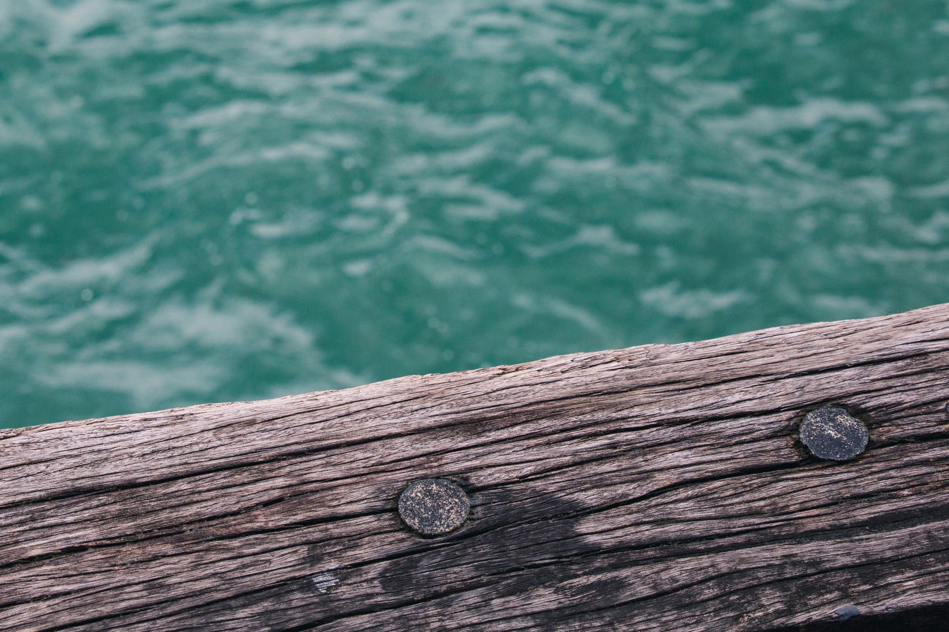 Close-up view of a rustic wooden pier with turquoise water in the background, highlighting texture and natural beauty.