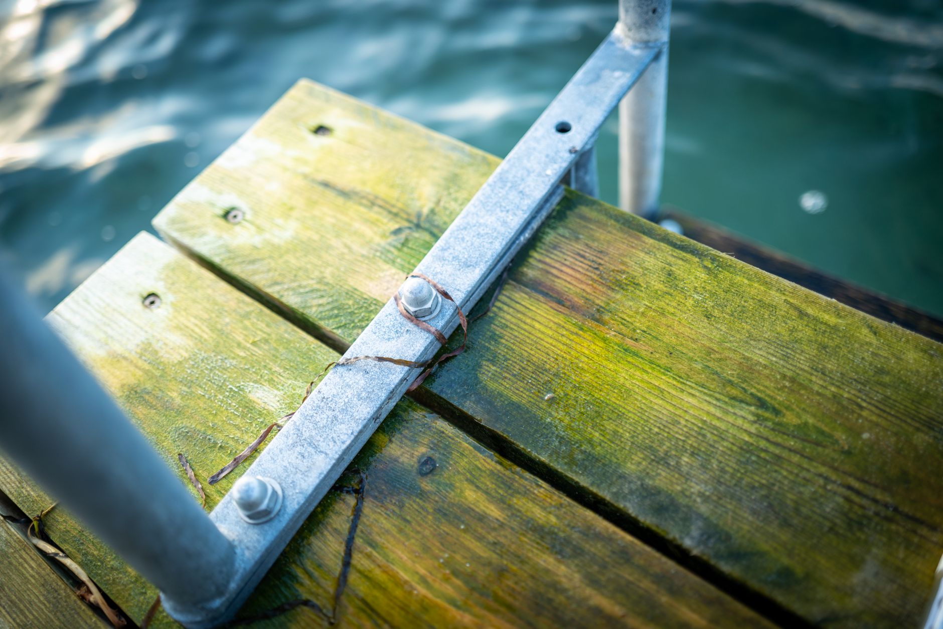 Close-up view of a wooden pier and metal railings with water backdrop. High angle shot.