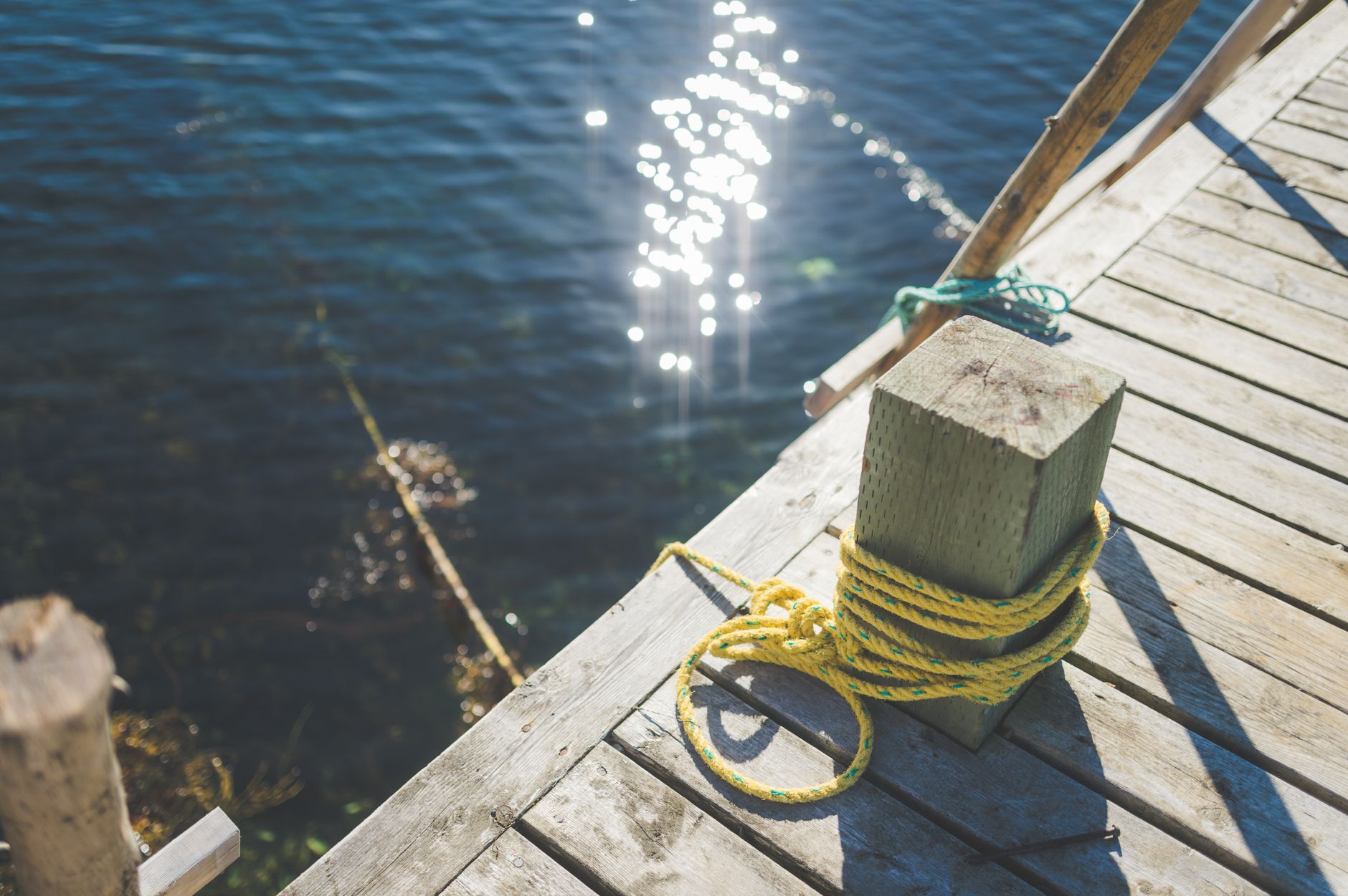 A serene view of a wooden dock with a yellow rope and sparkling blue water in the background.