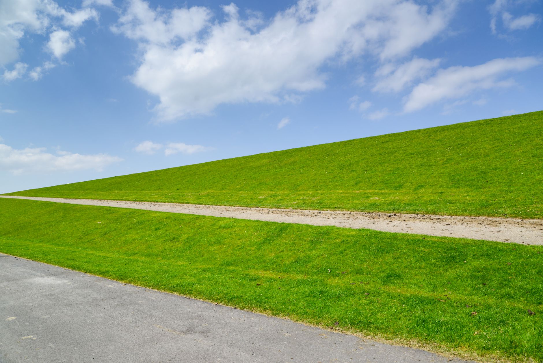 A picturesque view of a green hill and pathway under a bright blue sky with soft white clouds.
