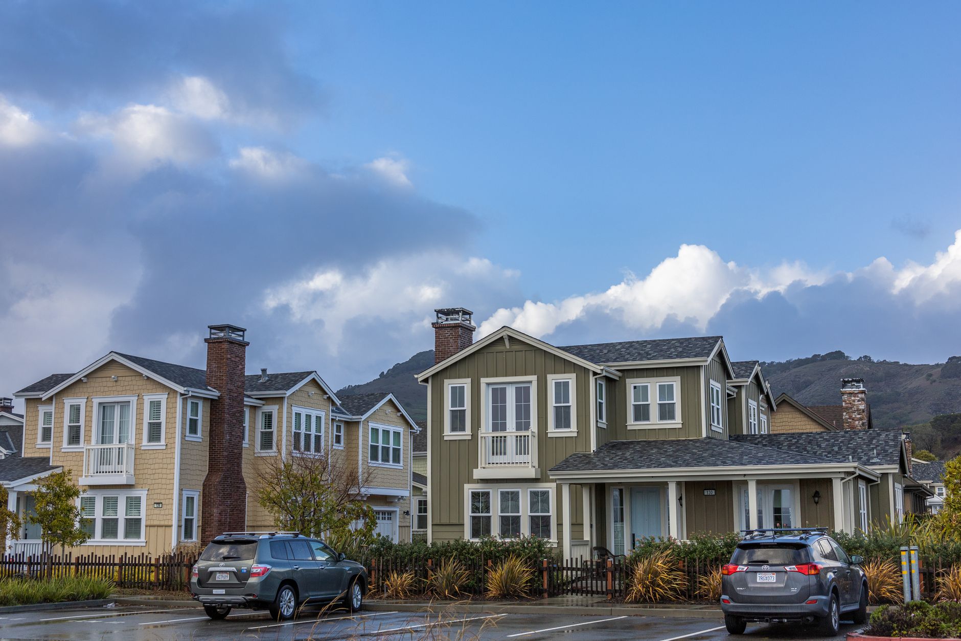 Picturesque suburban neighborhood with modern houses and parked cars under a partly cloudy sky.