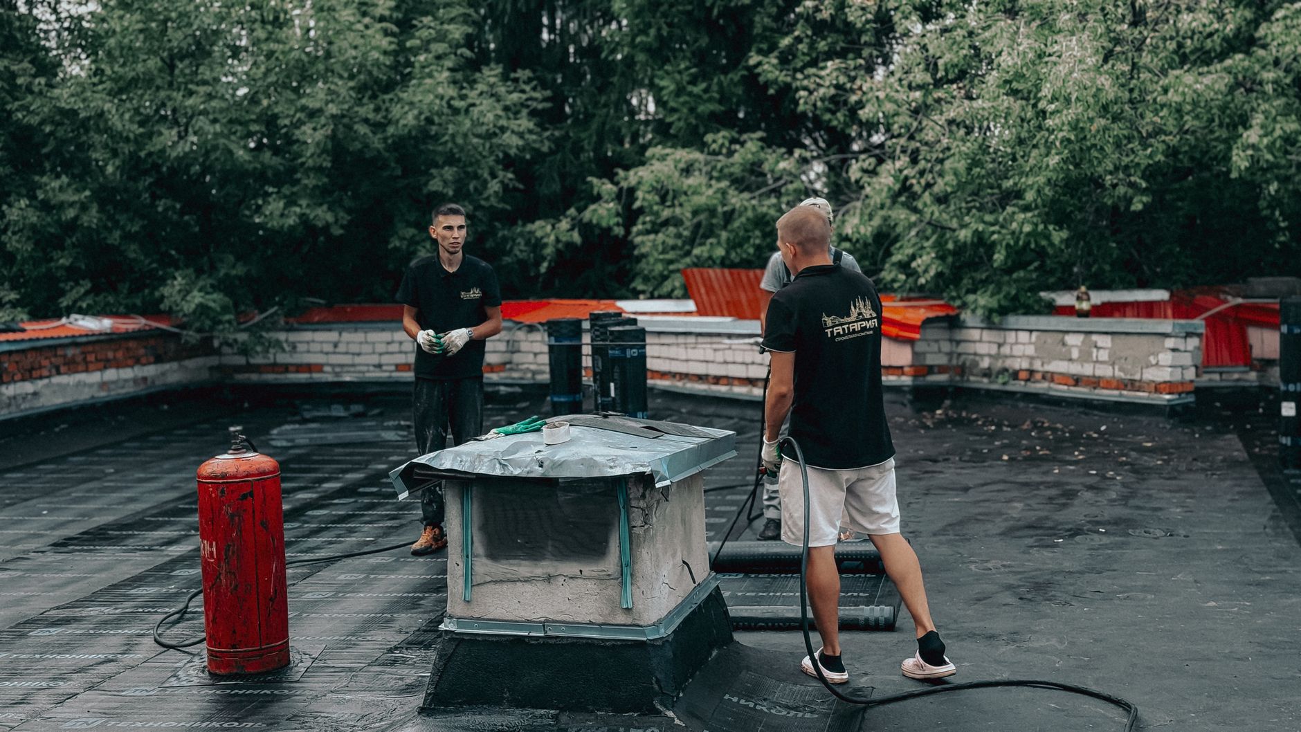Two workers are performing maintenance on a flat roof with equipment and tools.