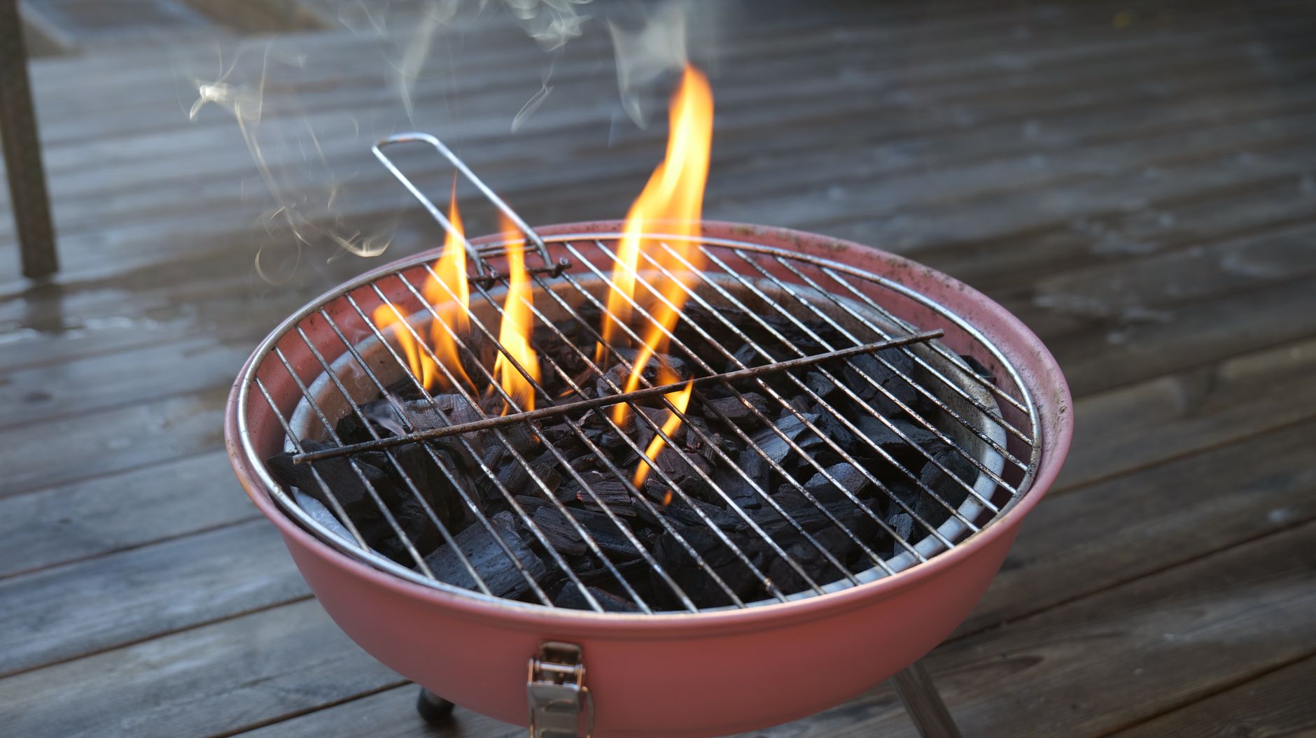 A charcoal grill with burning flames and smoke on a wooden deck, perfect for outdoor cooking.