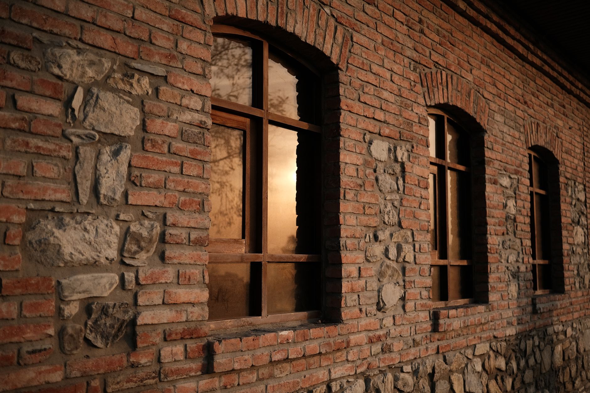 Brick wall with sunset reflections on wooden framed windows, capturing rustic charm.