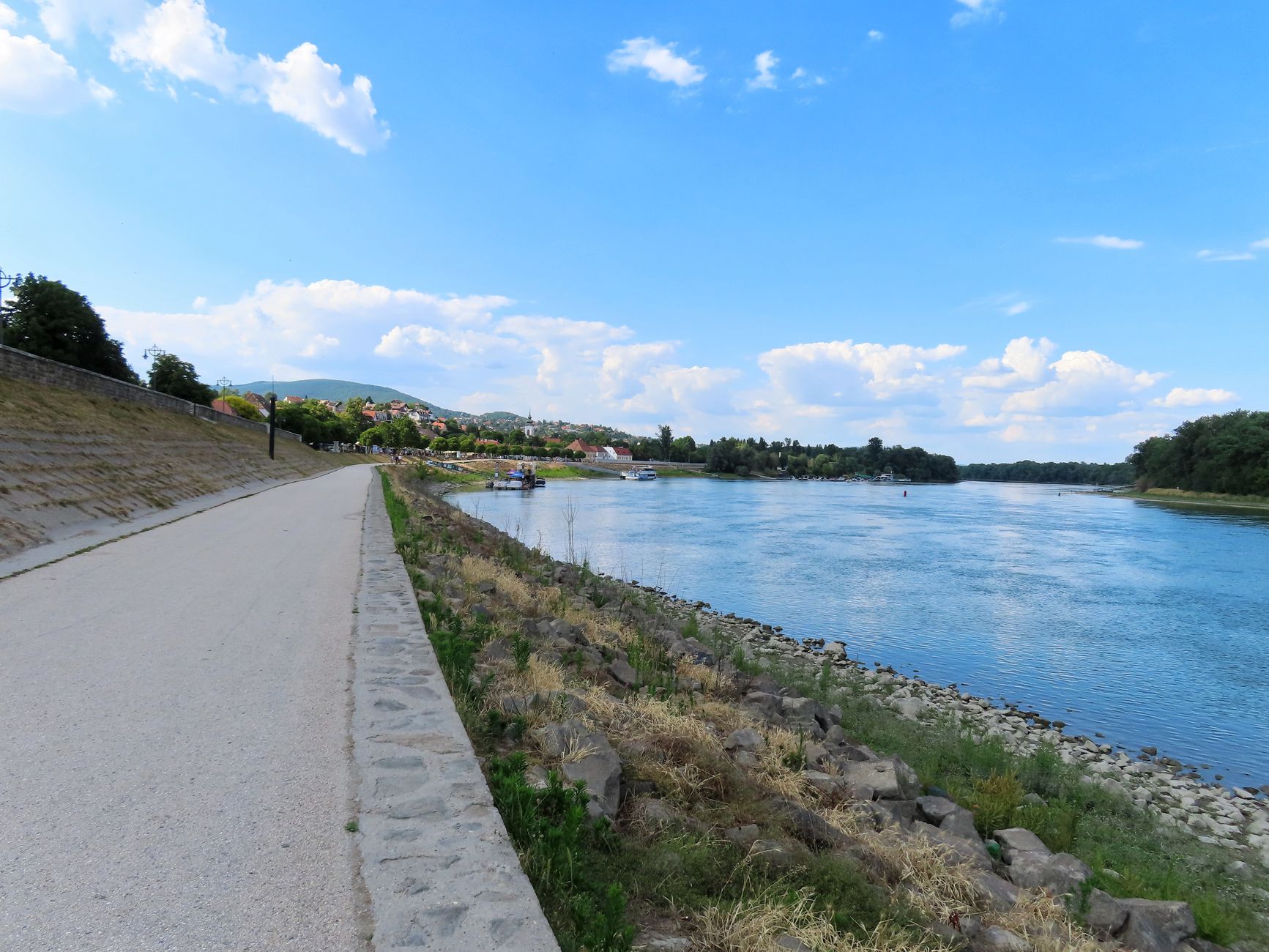 A scenic riverbank path under a bright blue sky, ideal for walks and relaxing outdoors.