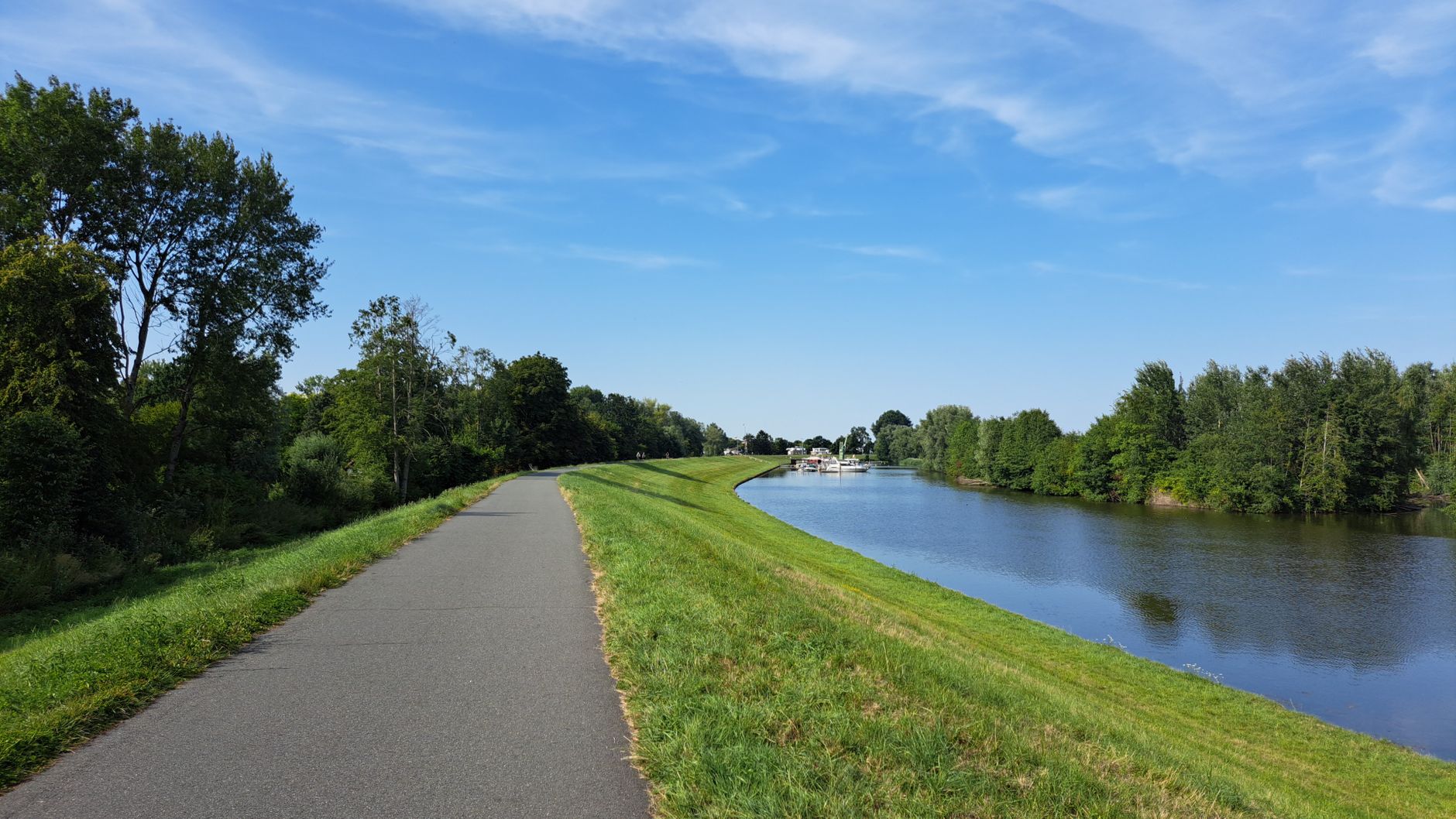 A tranquil riverside path ideal for a peaceful stroll or cycling under a clear blue sky.