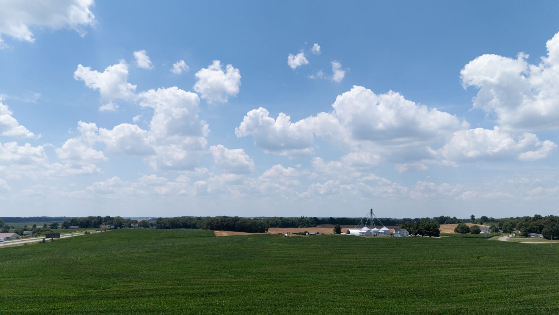 Wide view of a lush green farmland under a sky filled with fluffy clouds.